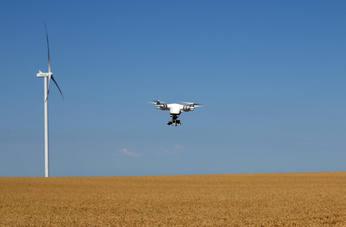 Drone flying over a field near a wind turbine
